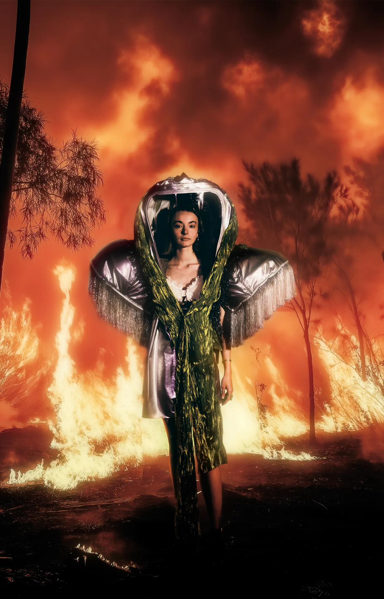 Model wearing a sculptural look before a burning landscape